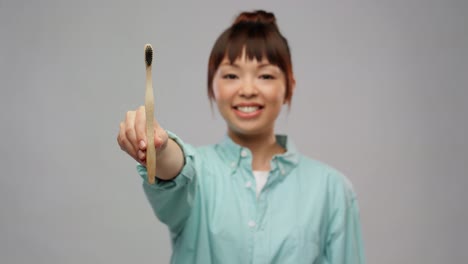 Smiling-Asian-Woman-with-Wooden-Toothbrush.dental-care,-oral-hygiene-and-people-concept-portrait-of-happy-smiling-young-asian-woman-in-turquoise-shirt-with-wooden-toothbrush-over-grey-background