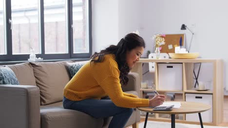 Asian-Woman-with-Papers-and-Calculator-at-Home.accounting,-taxes-and-finances-concept-young-asian-woman-with-papers-and-calculator-at-home