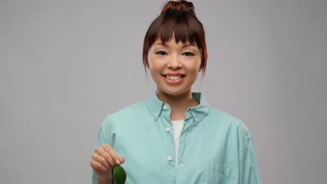 Happy-Asian-Woman-Holding-Car-Key-with-Green-Leaf.eco-living,-environment-and-sustainability-concept-portrait-of-happy-smiling-young-asian-woman-in-turquoise-shirt-holding-car-key-with-green-leaf-over-grey-background