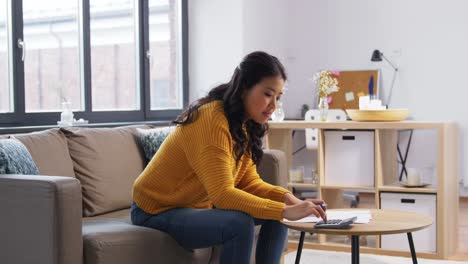 Asian-Woman-with-Papers-and-Calculator-at-Home.accounting,-taxes-and-finances-concept-young-asian-woman-with-papers-and-calculator-at-home