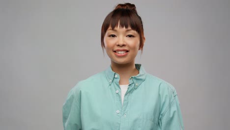 Smiling-Asian-Woman-with-Wooden-Toothbrush.dental-care,-oral-hygiene-and-people-concept-portrait-of-happy-smiling-young-asian-woman-in-turquoise-shirt-with-wooden-toothbrush-over-grey-background