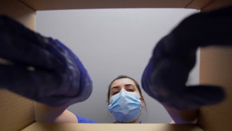 Woman-in-Mask-Packing-Camera-Into-Parcel-Box.delivery,-shipping-and-pandemic-concept-woman-in-protective-medical-mask-and-gloves-packing-digital-camera-and-lens-into-parcel-box