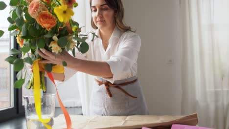 Professionelle-Floristin-In-Schwarzer-Schürze-Schneidet-Mit-Der-Schere-Geschenkpapier-Für-Einen-Blumenstrauß.-Professionelle-Floristin-In-Schwarzer-Schürze-Schneidet-Mit-Der-Schere-Geschenkpapier-Für-Einen-Blumenstrauß-Auf-Dem-Tisch-In-Einer-Floristikwerkstatt-Aus-Nächster-Nähe