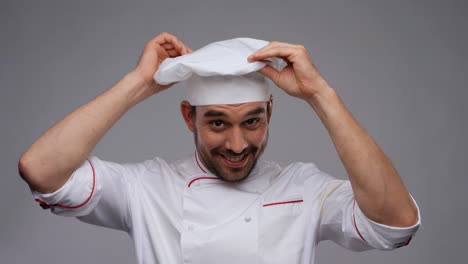 cooking,-culinary-and-people-concept--happy-smiling-male-chef-adjusting-toque-over-grey-background