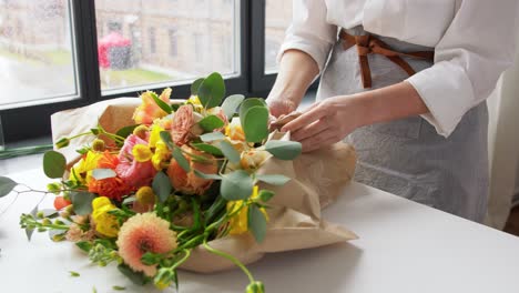 Professionelle-Floristin-In-Schwarzer-Schürze-Schneidet-Mit-Der-Schere-Geschenkpapier-Für-Einen-Blumenstrauß.-Professionelle-Floristin-In-Schwarzer-Schürze-Schneidet-Mit-Der-Schere-Geschenkpapier-Für-Einen-Blumenstrauß-Auf-Dem-Tisch-In-Einer-Floristikwerkstatt-Aus-Nächster-Nähe