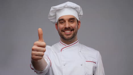 cooking,-culinary-and-people-concept--happy-smiling-male-chef-in-toque-showing-thumbs-up-over-grey-background