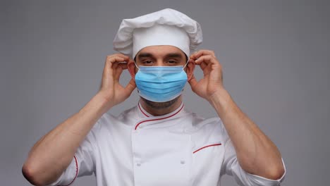 cooking,-culinary-and-pandemic-concept--male-chef-in-toque-wearing-face-protective-medical-mask-for-protection-from-virus-disease-over-grey-background