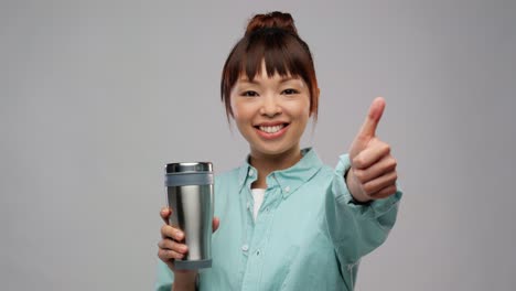 Mujer-Con-Taza-Térmica-O-Vaso-Mostrando-Los-Pulgares-Hacia-Arriba.Concepto-De-Sostenibilidad-Y-Personas.-Retrato-De-Una-Joven-Asiática-Con-Taza-Térmica-O-Vaso-Para-Bebidas-Calientes-Mostrando-Los-Pulgares-Hacia-Arriba-Sobre-Fondo-Gris.