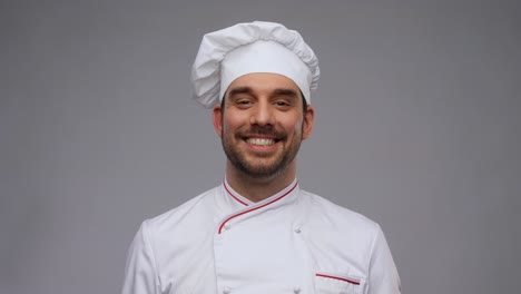 cooking,-culinary-and-people-concept--happy-smiling-male-chef-in-toque-and-jacket-over-grey-background