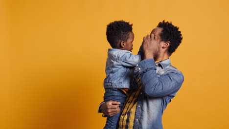 Playful-smiling-father-embracing-his-cute-infant-toddler-in-studio