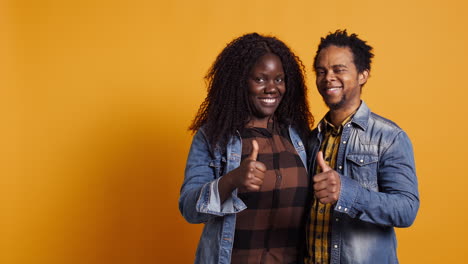 Sweet-african-american-couple-showing-thumbs-up-in-studio