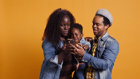 Familia-Sonriendo-Para-Selfies-En-Un-Teléfono-Inteligente-Con-Un-Niño-Sobre-Un-Fondo-Amarillo