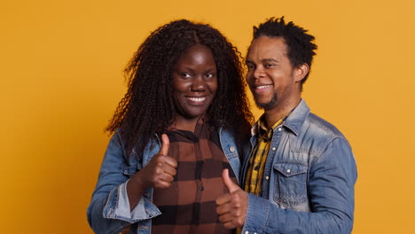 Sweet-african-american-couple-showing-thumbs-up-in-studio