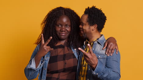 Cute-couple-showing-peace-sign-against-yellow-background