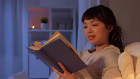 Mujer-Asiática-Joven-Leyendo-Un-Libro-En-La-Cama-En-Casa.-Gente,-Hora-De-Dormir-Y-Concepto-De-Descanso-Mujer-Asiática-Joven-Sonriente-Feliz-Leyendo-Un-Libro-En-La-Cama-En-Casa-Por-La-Noche