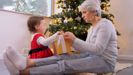 Großmutter-Und-Kleines-Mädchen-öffnen-Weihnachtsgeschenk.Weihnachten,-Feiertage-Und-Familienkonzept.-Glückliche-Großmutter-Und-Kleine-Enkelin-öffnen-Geschenkbox-Zu-Hause