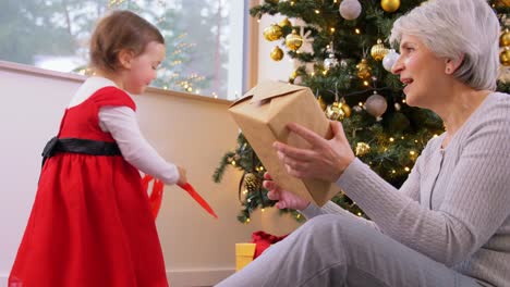 Grandmother-and-Baby-Girl-Opening-Christmas-Gift.christmas,-holidays-and-family-concept-happy-grandmother-and-baby-granddaughter-opening-gift-box-at-home