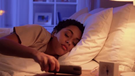 Mujer-Dormida-Que-Se-Despierta-Por-El-Teléfono-Por-La-Noche.-Tecnología,-Internet,-Comunicación-Y-Concepto-De-Personas.-Mujer-Afroamericana-Joven-Durmiendo-En-La-Cama-Y-Despertándose-Por-El-Teléfono-Inteligente-En-Casa-Por-La-Noche.