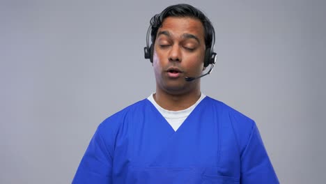 Indian-Doctor-in-Headset-Having-Conference-Call.healthcare,-medicine-and-communication-concept-indian-doctor-or-male-nurse-in-blue-uniform-and-headset-having-conference-call-over-grey-background