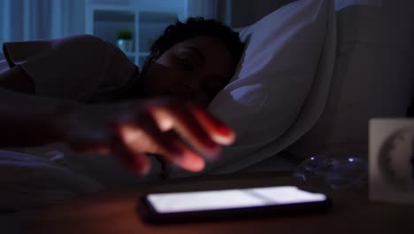 Mujer-Dormida-Que-Se-Despierta-Por-El-Teléfono-Por-La-Noche.-Tecnología,-Internet,-Comunicación-Y-Concepto-De-Personas.-Mujer-Afroamericana-Joven-Durmiendo-En-La-Cama-Y-Despertándose-Por-El-Teléfono-Inteligente-En-Casa-Por-La-Noche.