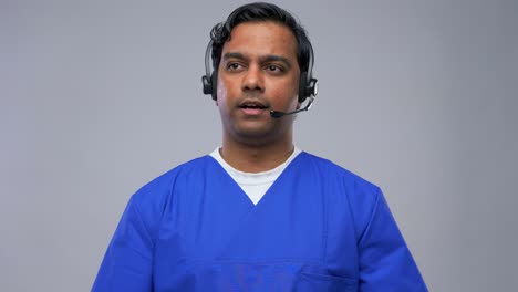 Indian-Doctor-in-Headset-Having-Conference-Call.healthcare,-medicine-and-communication-concept-indian-doctor-or-male-nurse-in-blue-uniform-and-headset-having-conference-call-over-grey-background