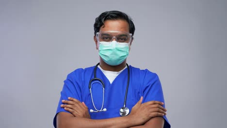 Médico-Indio-Con-Máscara-Poniéndose-Gafas-Protectoras.-Concepto-De-Salud,-Profesión-Y-Medicina.-Médico-Indio-O-Enfermero-Con-Uniforme-Azul-Y-Máscara-Médica-Protectora-Facial-Para-Protegerse-De-Enfermedades-Virales-Poniéndose-Gafas-Protectoras-Sobre-Fondo-Gris.