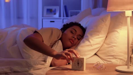 Woman-Awaking-Because-of-Alarm-Clock-at-Night.people,-bedtime-and-rest-concept-african-american-woman-awaking-because-of-alarm-clock-at-night