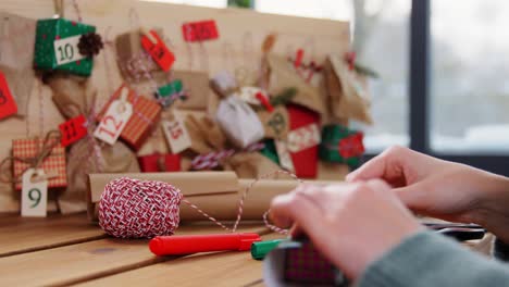 Hände,-Die-Zu-Hause-Einen-Weihnachts-Adventskalender-Basteln.-Winterferien,-Weihnachts--Und-Hobbykonzept-Hände,-Die-Eine-Geschenkbox-Mit-Etikett-An-Einen-Handgefertigten-Adventskalender-Zu-Hause-über-Schnee-Hängen