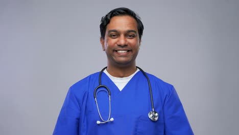 Indian-Male-Doctor-in-Blue-Uniform-Taking-Mask-Off.healthcare,-profession-and-medicine-concept-happy-smiling-indian-doctor-or-male-nurse-in-blue-uniform-taking-off-face-protective-medical-mask-for-protection-from-virus-disease-over-grey-background