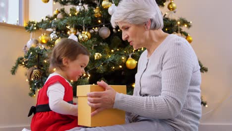 Großmutter-Und-Kleines-Mädchen-öffnen-Weihnachtsgeschenk.Weihnachten,-Feiertage-Und-Familienkonzept.-Glückliche-Großmutter-Und-Kleine-Enkelin-öffnen-Geschenkbox-Zu-Hause