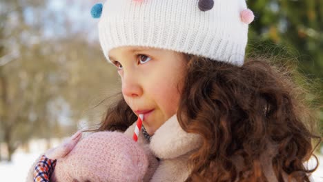 Niña-Bebiendo-Té-Caliente-Durante-Una-Caminata-En-Invierno.-Toma-Aérea-En-ángulo-Bajo-De-Una-Linda-Niña-Con-Gorro,-Parka-Y-Guantes-Bebiendo-Té-Caliente-De-Una-Taza-De-Acero-Inoxidable-Mientras-Camina-Por-El-Bosque-En-Un-Día-Soleado-De-Invierno.