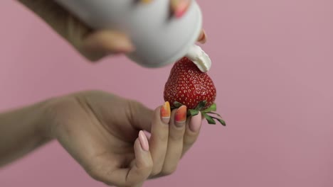 Woman-hand-holds-strawberry-and-squeeze-out-whipped-cream-on-top-of-the-berry