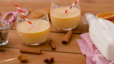 Glasses-of-Eggnog,-Ingredients-and-Spices-on-Wood.christmas,-winter-holidays-and-seasonal-drinks-concept-–-glasses-with-eggnog,-ingredients-and-aromatic-spices-on-wooden-board-over-snow-falling