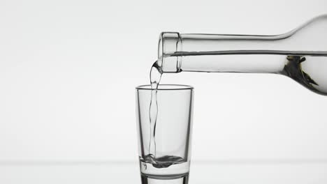 Pouring-up-shot-of-vodka-from-a-bottle-into-glass.-White-background