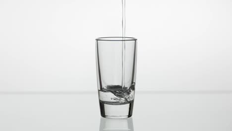 Pouring-up-shot-of-vodka-into-drinking-glass.-Slow-motion.-White-background