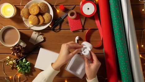 Woman-Wrapping-Earphones-for-Christmas-Gift.holidays,-new-year-and-christmas-concept-–-woman-packing-wireless-earphones-for-gift-into-green-wrapping-paper-over-snow