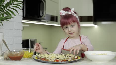 Cooking.-Little-child-in-apron-adding-grated-cheese-to-raw-pizza-in-kitchen