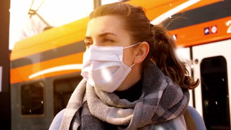 Woman-in-Protective-Face-Mask-at-Railway-Station.health,-safety-and-pandemic-concept-–-young-woman-in-protective-face-mask-with-travel-bag-walking-along-empty-railway-station