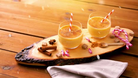 Glasses-of-Eggnog,-Ingredients-and-Spices-on-Wood.christmas,-winter-holidays-and-seasonal-drinks-concept-–-glasses-with-eggnog,-ingredients-and-aromatic-spices-on-wooden-board-over-snow-falling