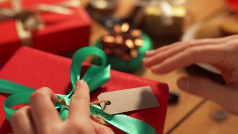 Hands-Attaching-Name-Tag-To-Christmas-Gift.holidays,-new-year-and-christmas-concept-–-hands-packing-gift-box,-attaching-tag-and-writing-receiver-name-at-home-over-snow