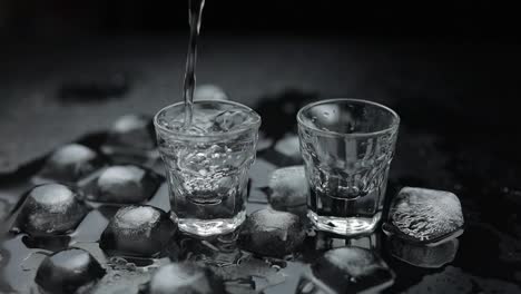 Pouring-up-shots-of-vodka-from-a-bottle-into-glass.-Black-background