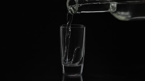 Pouring-up-shot-of-vodka-from-a-bottle-into-glass.-Black-background