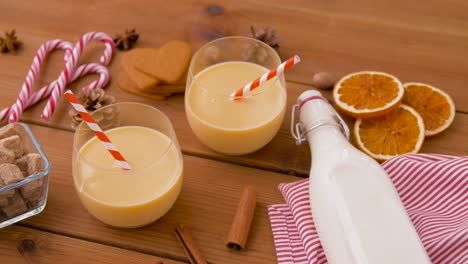 Glasses-of-Eggnog,-Ingredients-and-Spices-on-Wood.christmas,-winter-holidays-and-seasonal-drinks-concept-–-glasses-with-eggnog,-ingredients-and-aromatic-spices-on-wooden-board-over-snow-falling