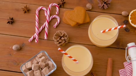 Glasses-of-Eggnog,-Ingredients-and-Spices-on-Wood.christmas,-winter-holidays-and-seasonal-drinks-concept-–-glasses-with-eggnog,-ingredients-and-aromatic-spices-on-wooden-board-over-snow-falling