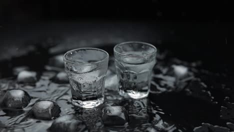 Add-ice-cubes-to-shot-of-vodka-in-glass-against-black-background.-Alcohol-drink