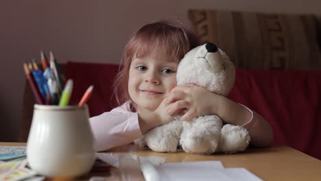 Cute-small-child-girl-sitting-at-home-playing-and-hugging-her-teddy-bear-toy