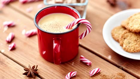 Becher-Eierlikör-Mit-Zuckerstange-Und-Keksen-Auf-Dem-Tisch.-Weihnachts--Und-Saisonales-Getränkekonzept-–-Schnee-Fällt-über-Einen-Roten-Becher-Eierlikör-Mit-Zuckerstange-Und-Keksen-Auf-Einem-Holztisch