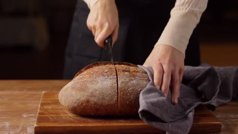 Female-Baker-Cutting-Homemade-Bread-at-Bakery.food-cooking,-baking-and-people-concept-–-female-baker-with-knife-cutting-loaf-of-bread-to-slices-at-bakery-or-kitchen