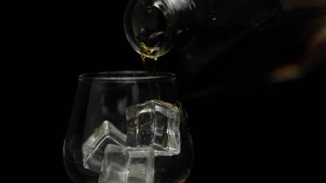 Pouring-alcohol-drink-whiskey,-cognac-into-glass.-Black-background.-Slow-motion