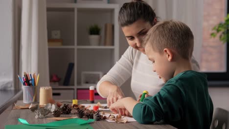 Madre-E-Hijo-Haciendo-Dibujos-De-Hojas-De-Otoño.-Concepto-De-Familia,-Creatividad-Y-Manualidades:-Madre-E-Hijo-Pequeño-Con-Barras-De-Pegamento-Y-Papel-Haciendo-Dibujos-De-Hojas-Secas-De-Otoño,-Piñas-Y-Castañas-En-Casa